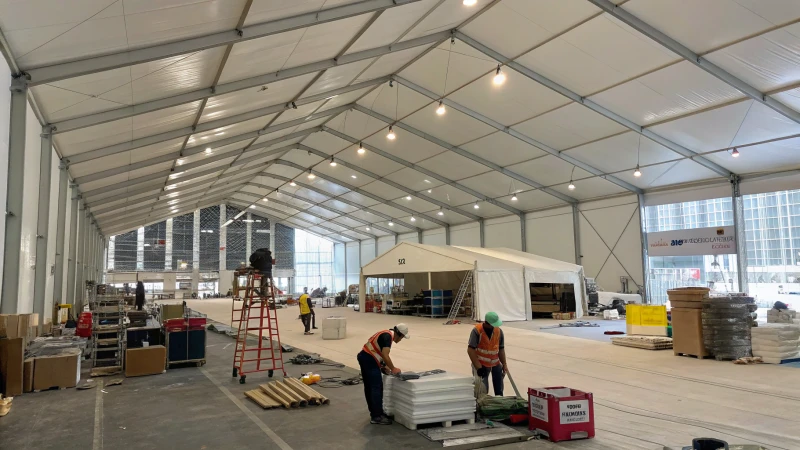 A large white industrial tent on a construction site with workers and equipment.