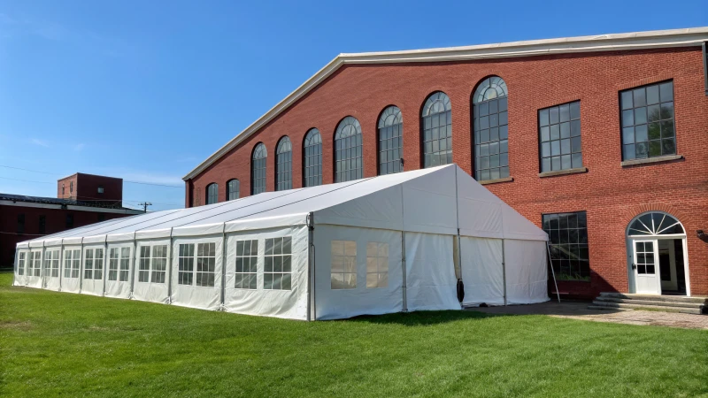 A large industrial tent next to a traditional brick building on a grassy area.