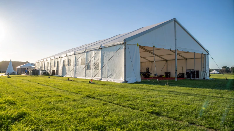 Large white warehouse tent set up in a grassy area with equipment around.